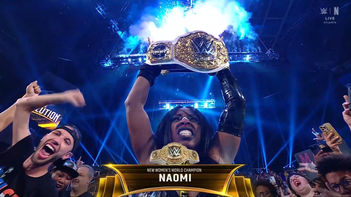 Naomi holding up the Women's World Title as fireworks erupt above her head and fans celebrate around her
