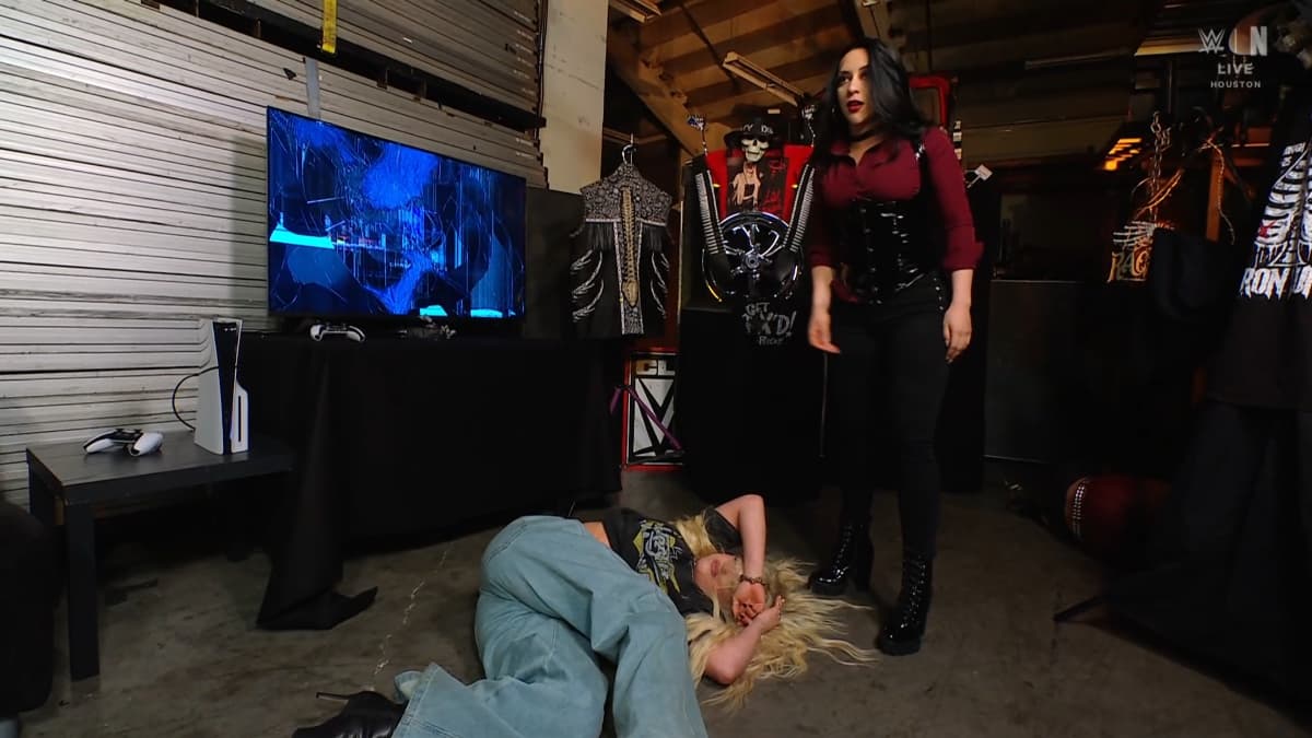 Stephanie Vaquer standing over Liv Morgan, who is lay on the cement as a smashed TV is behind them both
